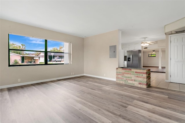 unfurnished living room with electric panel, a ceiling fan, light wood-type flooring, and baseboards