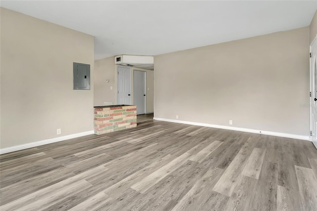 spare room featuring electric panel, baseboards, and wood finished floors