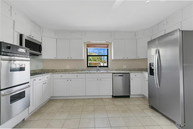 kitchen with a sink, stainless steel appliances, light stone counters, and white cabinets