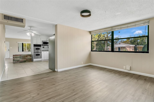 unfurnished room with light wood-type flooring, visible vents, and a textured ceiling