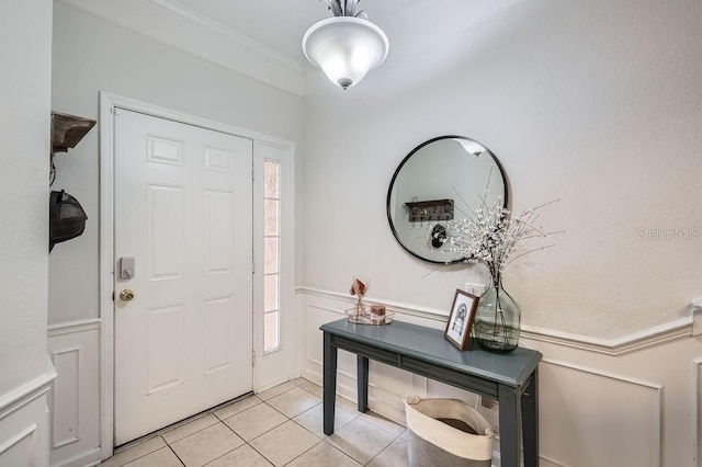 foyer featuring light tile patterned flooring, a wainscoted wall, a decorative wall, and crown molding