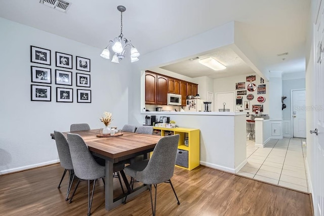 dining space featuring visible vents, baseboards, an inviting chandelier, and light wood-style flooring