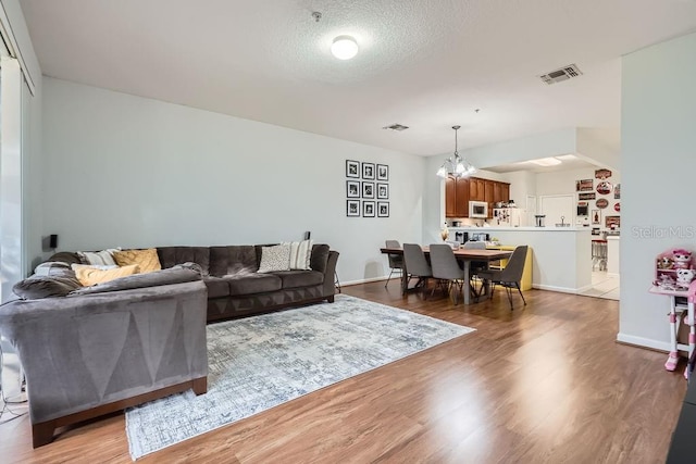 living area with a textured ceiling, wood finished floors, visible vents, and a chandelier