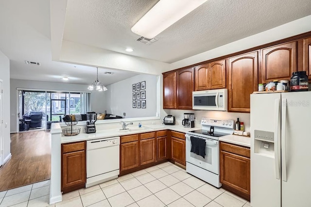 kitchen featuring white appliances, light tile patterned floors, visible vents, a peninsula, and a sink