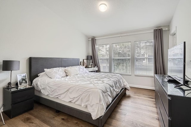 bedroom with vaulted ceiling, wood finished floors, and baseboards