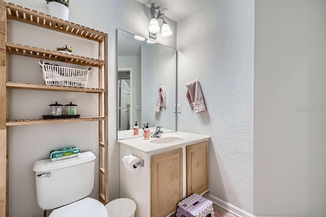 bathroom with vanity, toilet, and a textured wall
