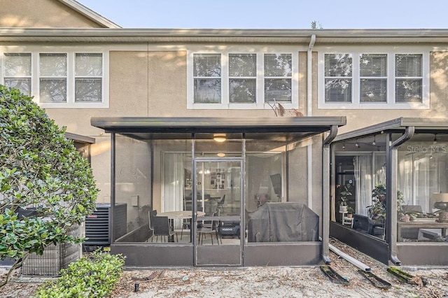 rear view of property with cooling unit, a sunroom, and stucco siding