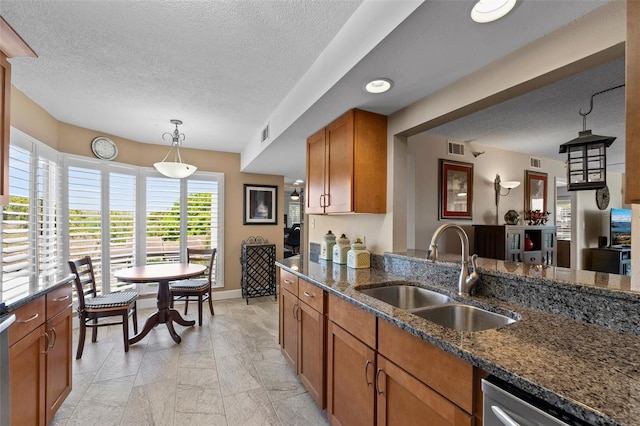 kitchen with a sink, dark stone countertops, stainless steel dishwasher, brown cabinetry, and hanging light fixtures