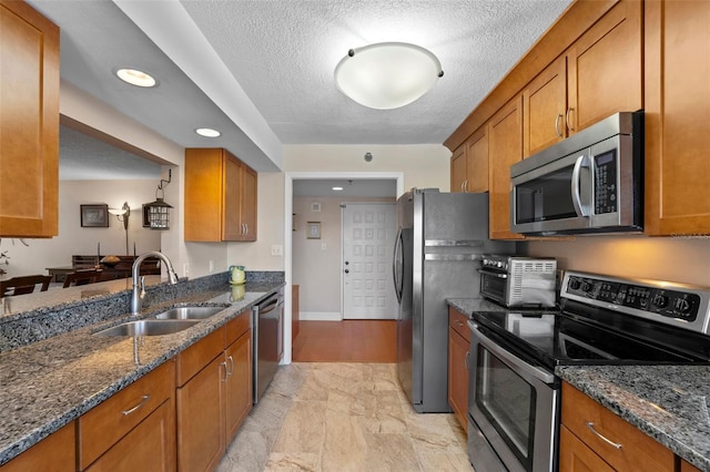 kitchen with brown cabinetry, stainless steel appliances, dark stone counters, and a sink