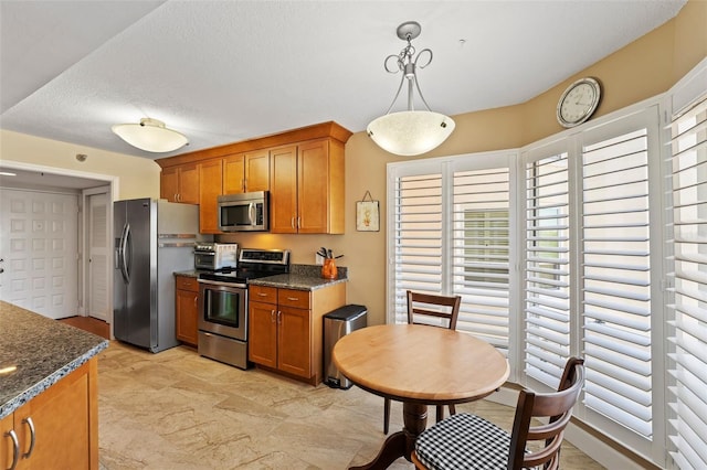 kitchen with brown cabinetry, hanging light fixtures, stainless steel appliances, and dark stone counters