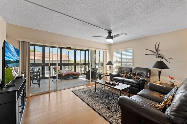 living area featuring a textured ceiling, light wood-type flooring, and ceiling fan