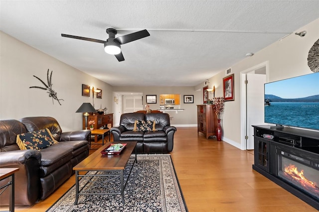 living room with a glass covered fireplace, visible vents, a textured ceiling, and light wood-style flooring