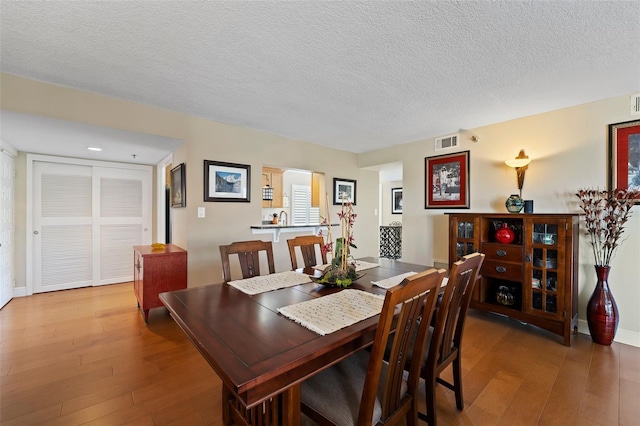 dining space with visible vents, baseboards, a textured ceiling, and wood finished floors