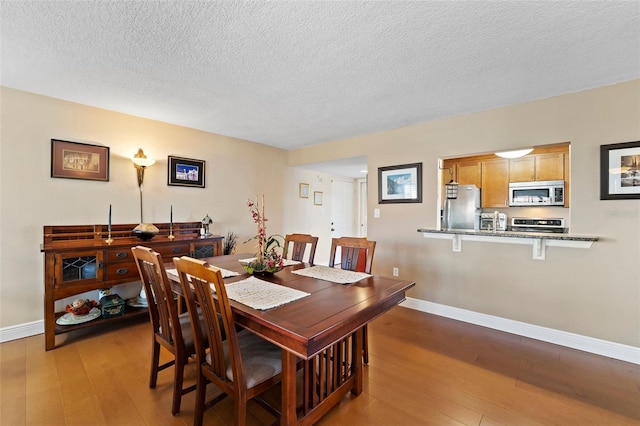 dining space featuring a textured ceiling, baseboards, and hardwood / wood-style floors