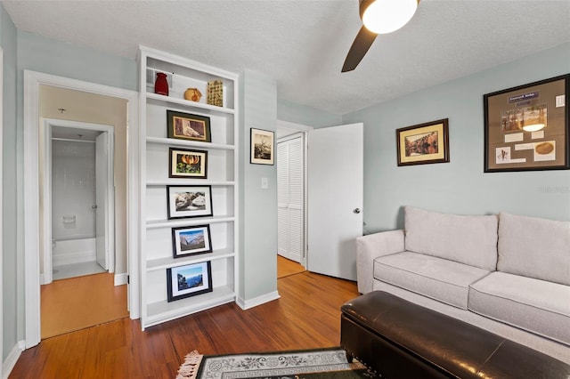 living area with wood finished floors, baseboards, ceiling fan, a textured ceiling, and a large fireplace