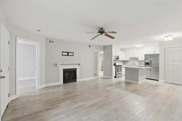 unfurnished living room with a ceiling fan, visible vents, light wood finished floors, baseboards, and a tiled fireplace