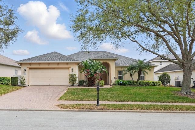 view of front of property featuring central air condition unit, stucco siding, a front lawn, decorative driveway, and a garage