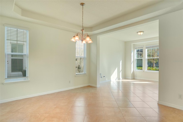 empty room with light tile patterned floors, a tray ceiling, and a healthy amount of sunlight