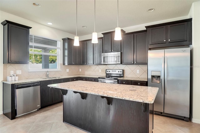 kitchen featuring light stone counters, a kitchen island, a sink, stainless steel appliances, and a kitchen bar