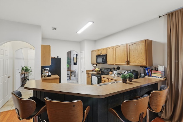 kitchen featuring visible vents, a kitchen breakfast bar, arched walkways, black appliances, and a sink