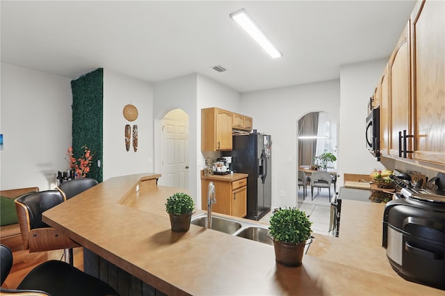 kitchen with visible vents, light brown cabinets, a kitchen bar, black appliances, and a sink