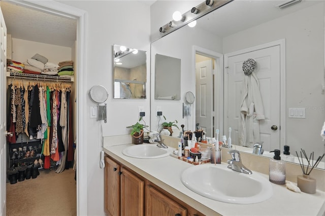 bathroom featuring a walk in closet, double vanity, visible vents, and a sink