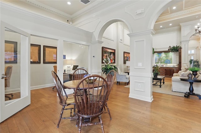 dining area with a towering ceiling, light wood-type flooring, ornate columns, and ornamental molding