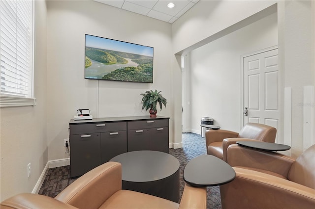 living area with a drop ceiling and baseboards