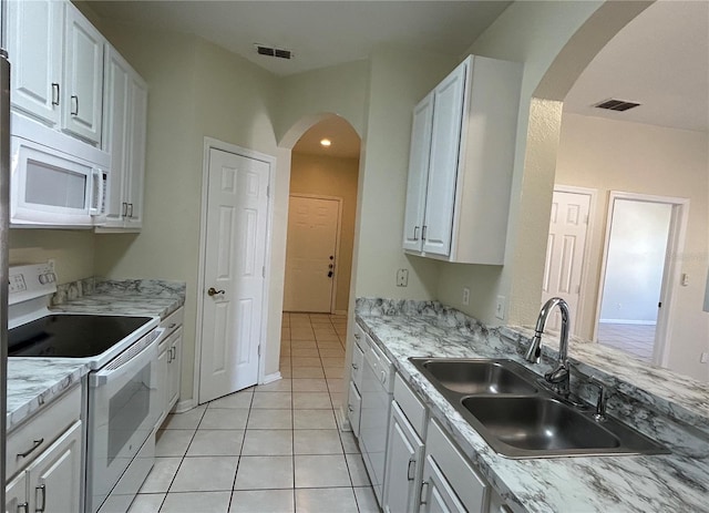 kitchen with white appliances, light tile patterned floors, visible vents, a sink, and white cabinetry