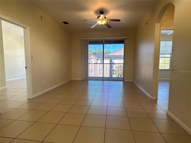 spare room with light tile patterned floors, arched walkways, baseboards, and a ceiling fan