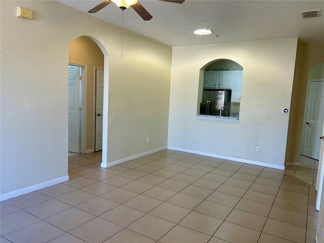 empty room featuring light tile patterned floors, visible vents, baseboards, and a ceiling fan