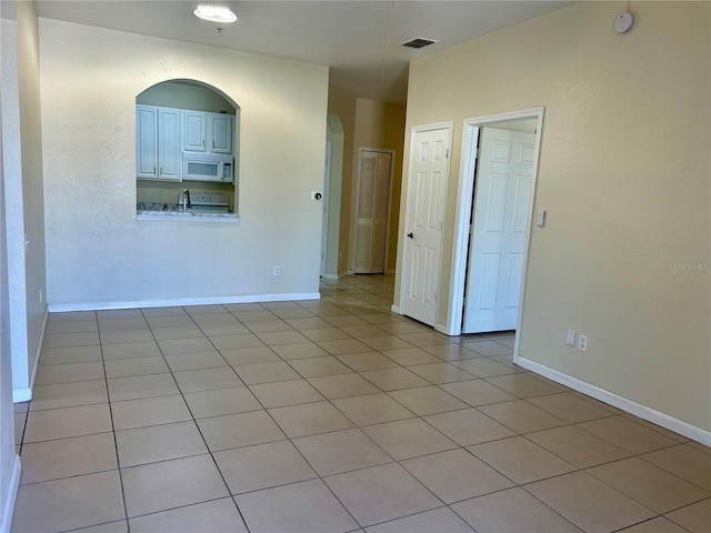 unfurnished room featuring arched walkways, visible vents, baseboards, and light tile patterned floors