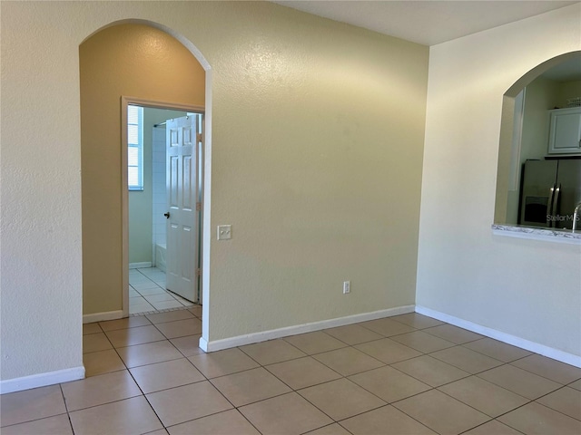 unfurnished room featuring light tile patterned floors, arched walkways, and baseboards