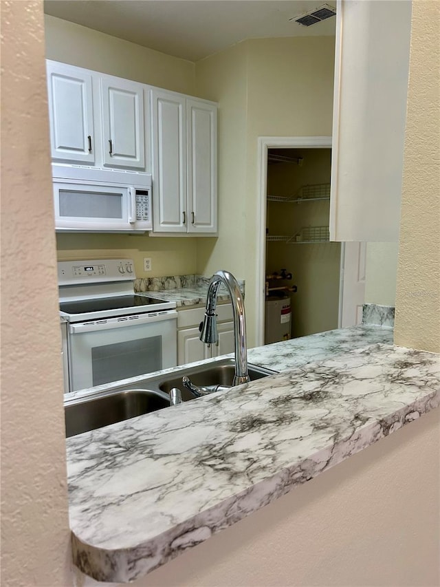 kitchen with white cabinetry, white appliances, visible vents, and a sink