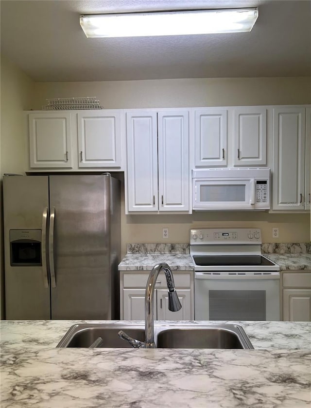 kitchen featuring a sink, white appliances, light stone counters, and white cabinetry