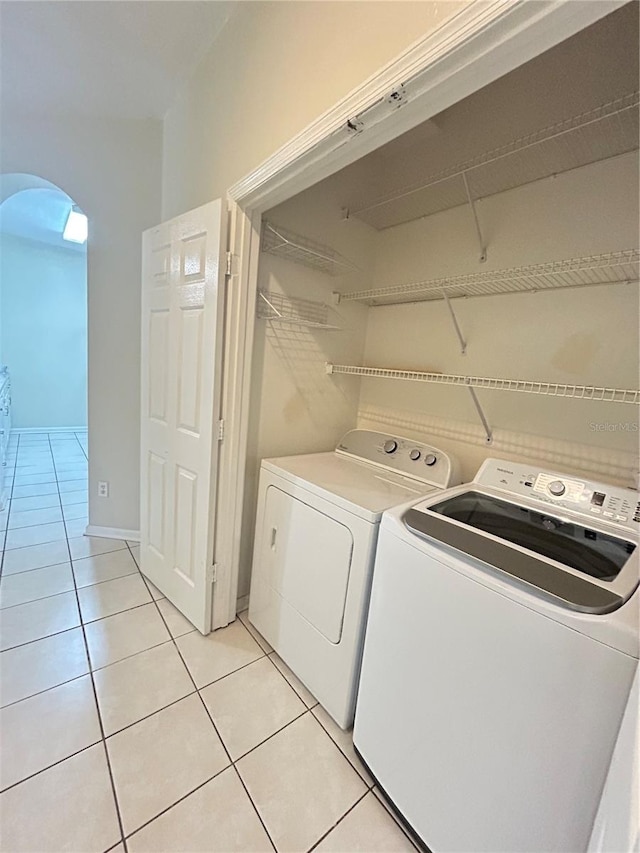 clothes washing area featuring light tile patterned floors, arched walkways, washing machine and dryer, and laundry area