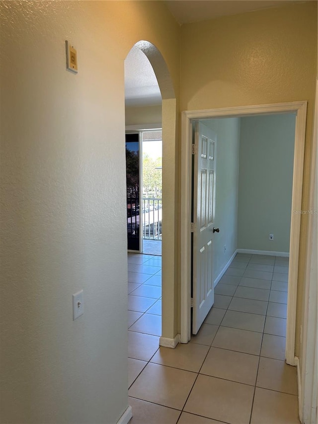 hall with light tile patterned floors, baseboards, arched walkways, and a textured wall