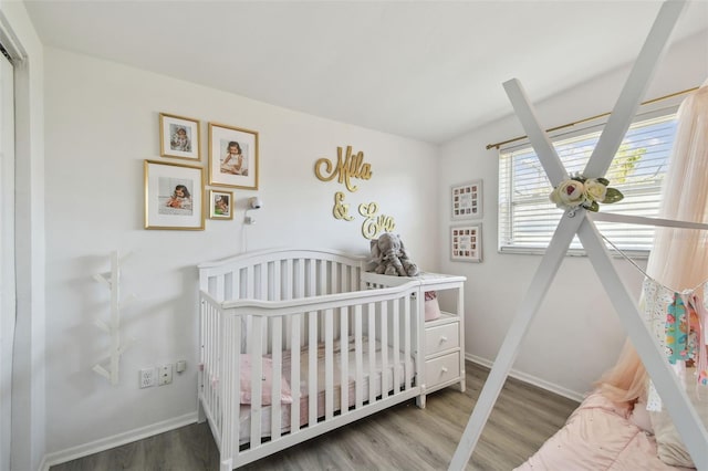 bedroom featuring a crib, baseboards, and wood finished floors