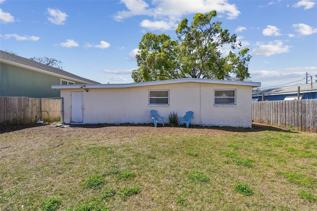 rear view of property featuring stucco siding, a lawn, and fence