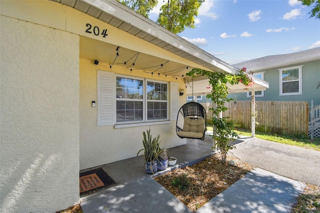 entrance to property featuring fence and stucco siding