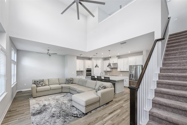 living room with stairway, baseboards, light wood finished floors, ceiling fan, and a towering ceiling