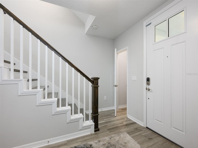 entrance foyer with stairway, baseboards, light wood finished floors, and a textured ceiling