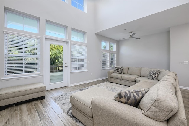 living area featuring ceiling fan, a high ceiling, baseboards, and wood finished floors