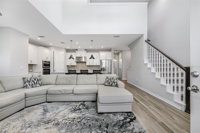 living area featuring light wood-type flooring, visible vents, baseboards, a towering ceiling, and stairs