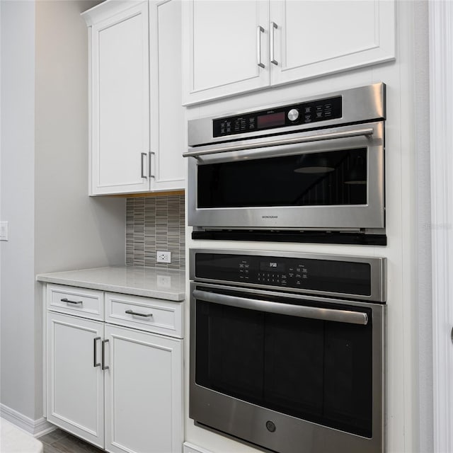 kitchen featuring white cabinetry, baseboards, tasteful backsplash, and stainless steel double oven