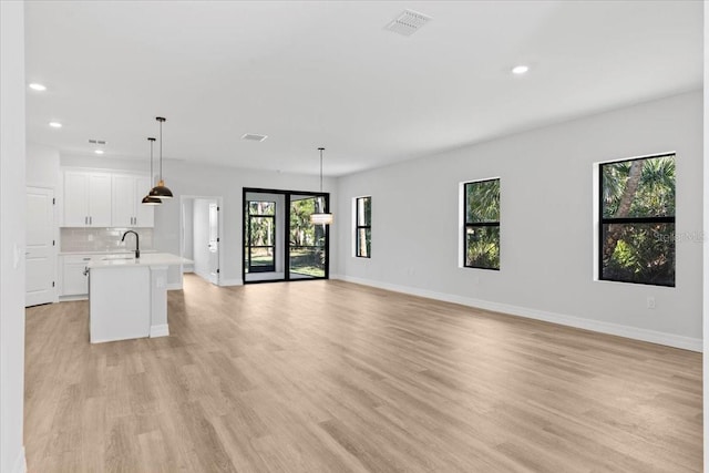 unfurnished living room with recessed lighting, light wood-style floors, baseboards, and a sink