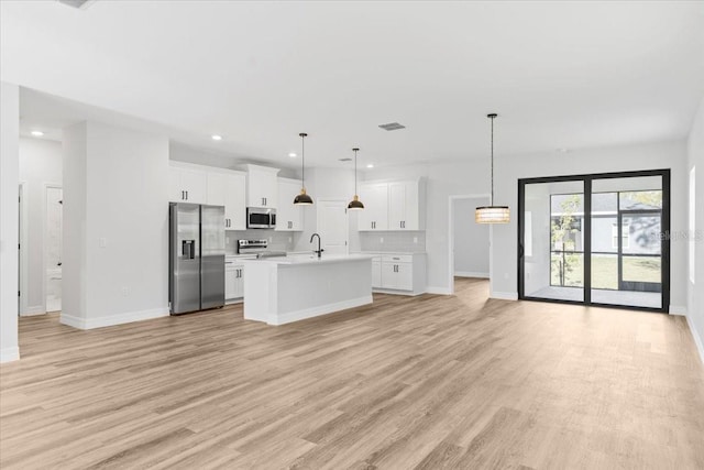 kitchen featuring open floor plan, an island with sink, light countertops, light wood-style flooring, and appliances with stainless steel finishes