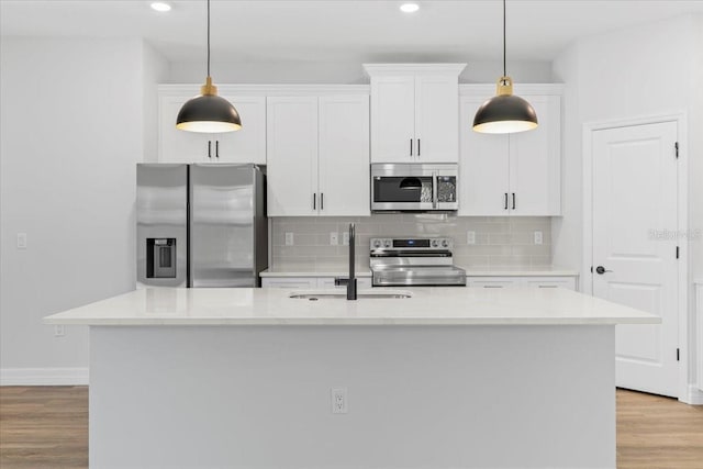 kitchen with a center island with sink, light wood-style flooring, white cabinets, stainless steel appliances, and a sink