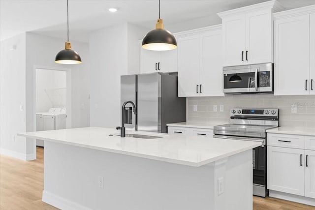 kitchen with tasteful backsplash, washer and clothes dryer, a center island with sink, light wood-style flooring, and appliances with stainless steel finishes