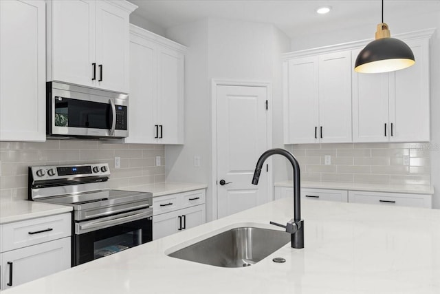 kitchen featuring pendant lighting, light countertops, appliances with stainless steel finishes, white cabinetry, and a sink